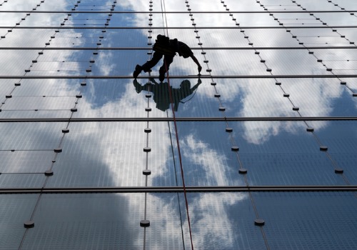 A window cleaner on a skyscraper offers commercial window cleaning & building maintenance services from All Window Cleaning Services, part of their complete commercial cleaning services