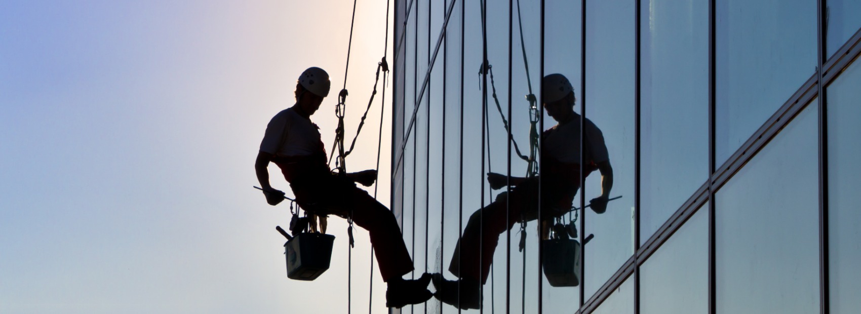 A worker from All Window Cleaning Services provides exterior cleaning services at sunset